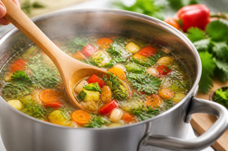 Kochlöffel in Topf mit bunter Gemüsesuppe, symbolisiert gesunde Ernährung